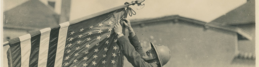 Sepia photograph of a WWI soldier hanging an American flag