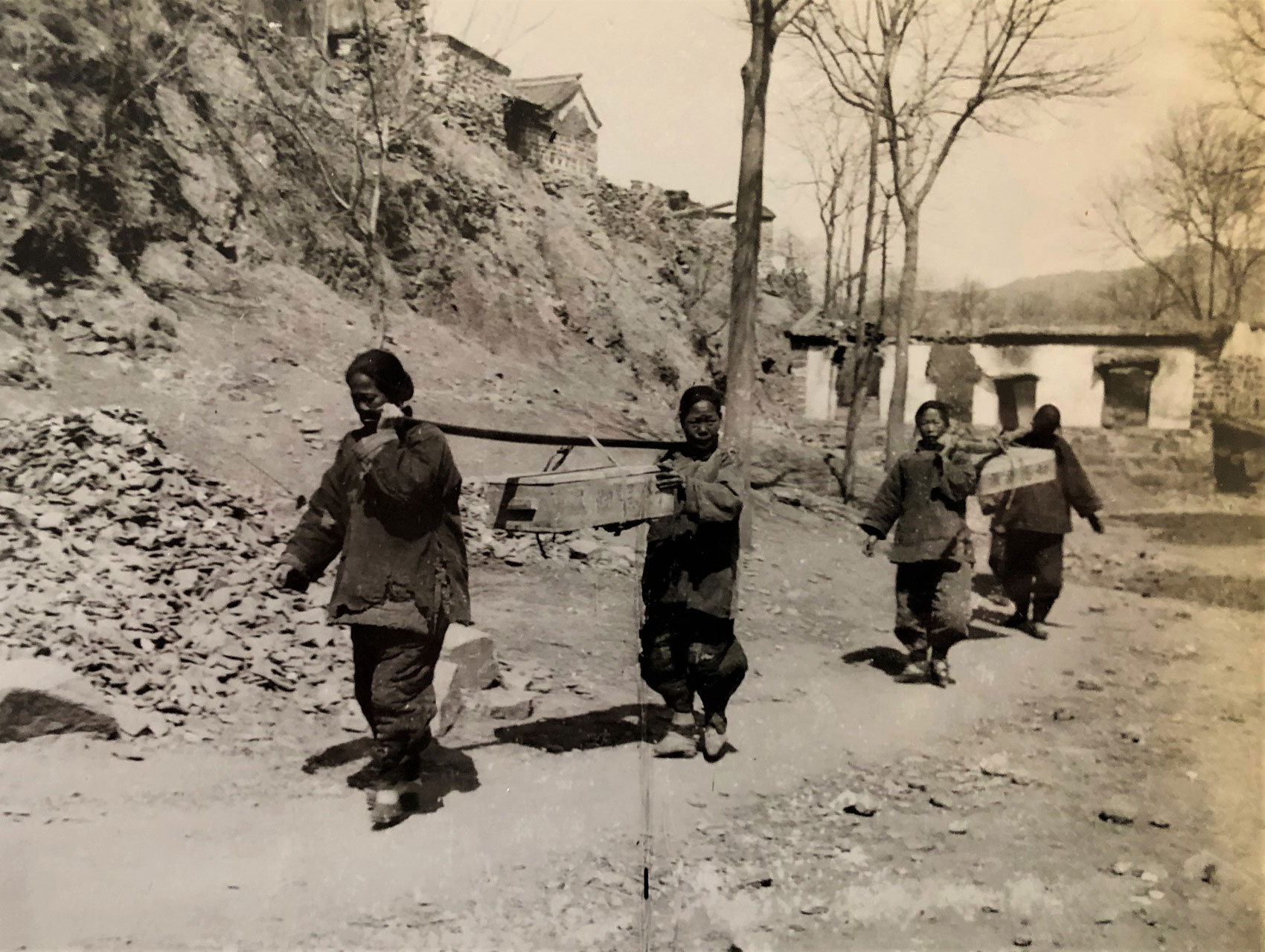 Black and white photo of people walking on a dirt trail. Sha Fei papers.