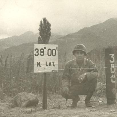 Black and white photo Kay K. Sasaki in US military uniform posing next to 38' 00" N. Lat. sign