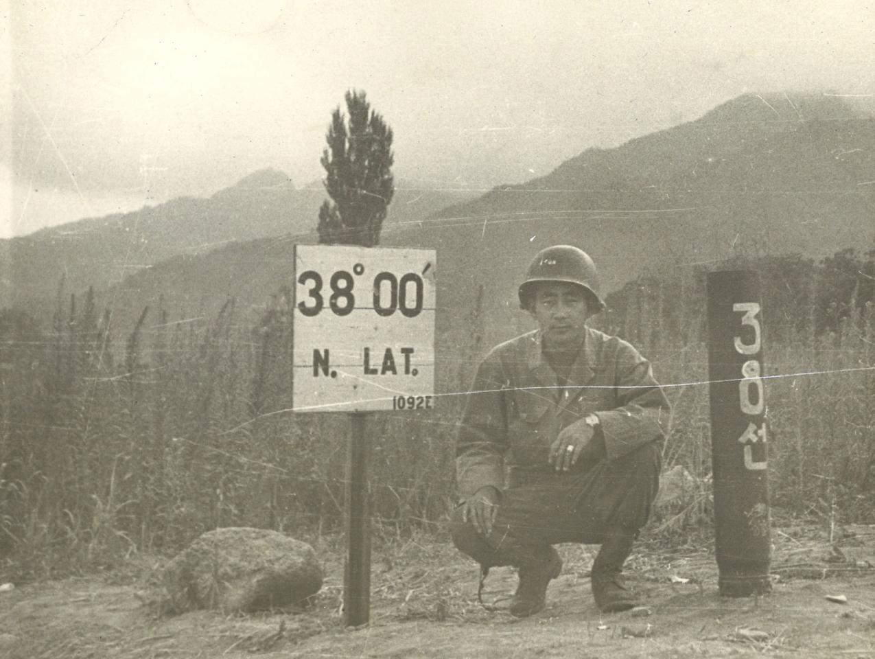 Black and white photo Kay K. Sasaki in US military uniform posing next to 38' 00" N. Lat. sign