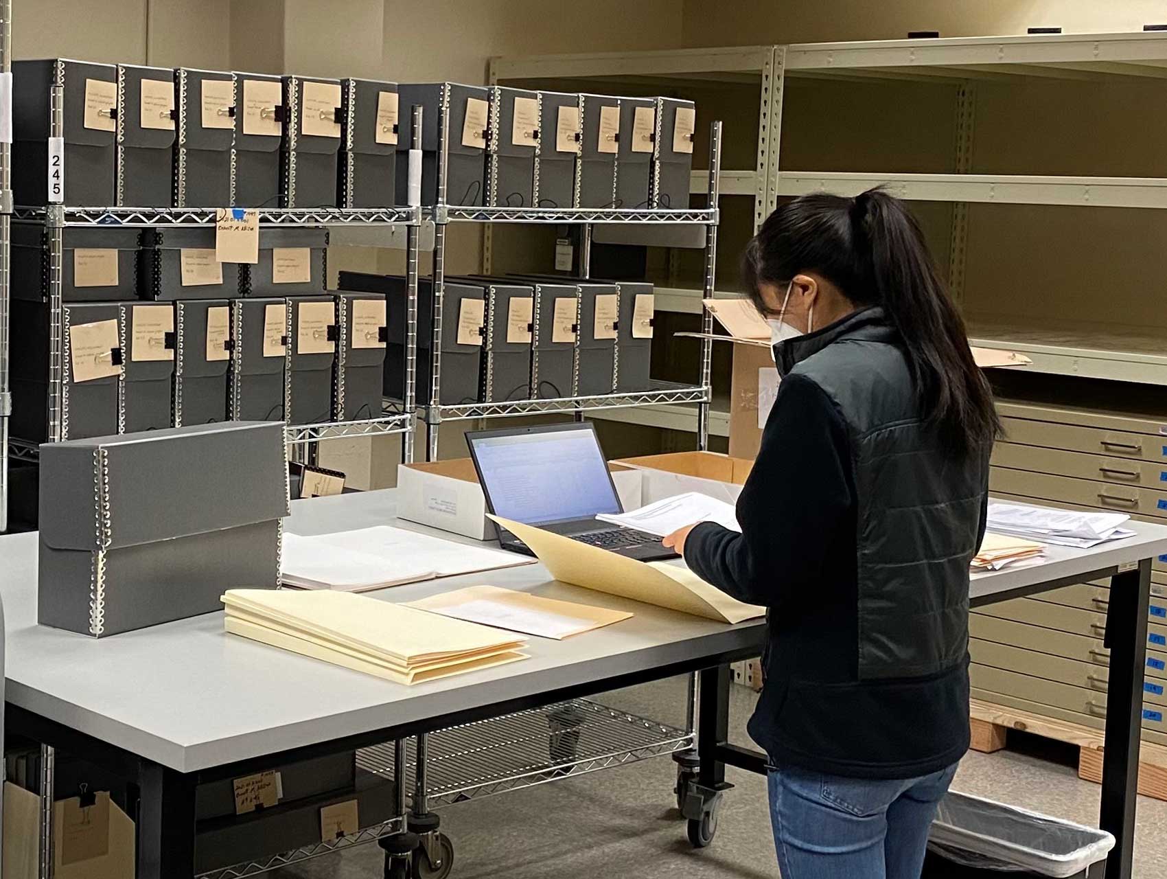 Jessica Y standing in front of a table with documents, laptop, and manuscript boxes