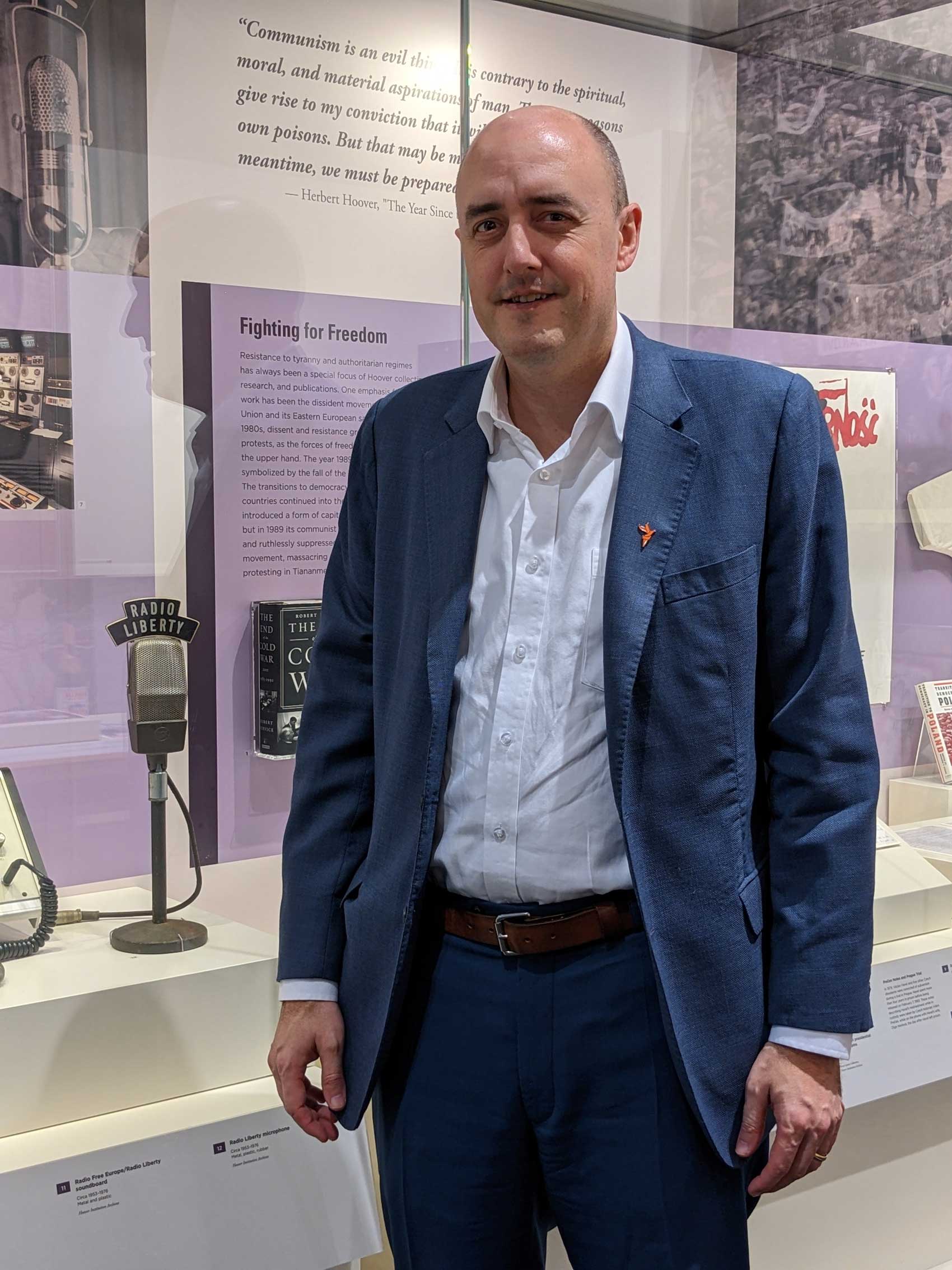 Jamie Fly, president of Radio Free Europe/Radio Liberty visiting Hoover Tower gallery stands next to RFE/FL microphone