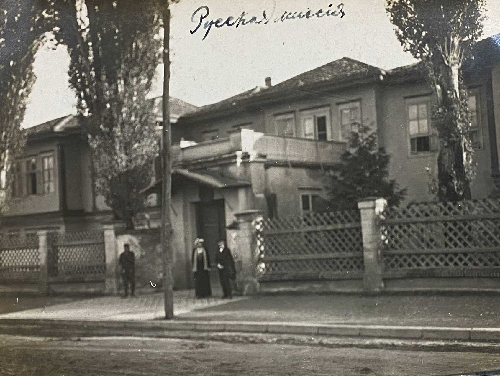 Black and white photo of 2 people standing in front of a 2 story building.
