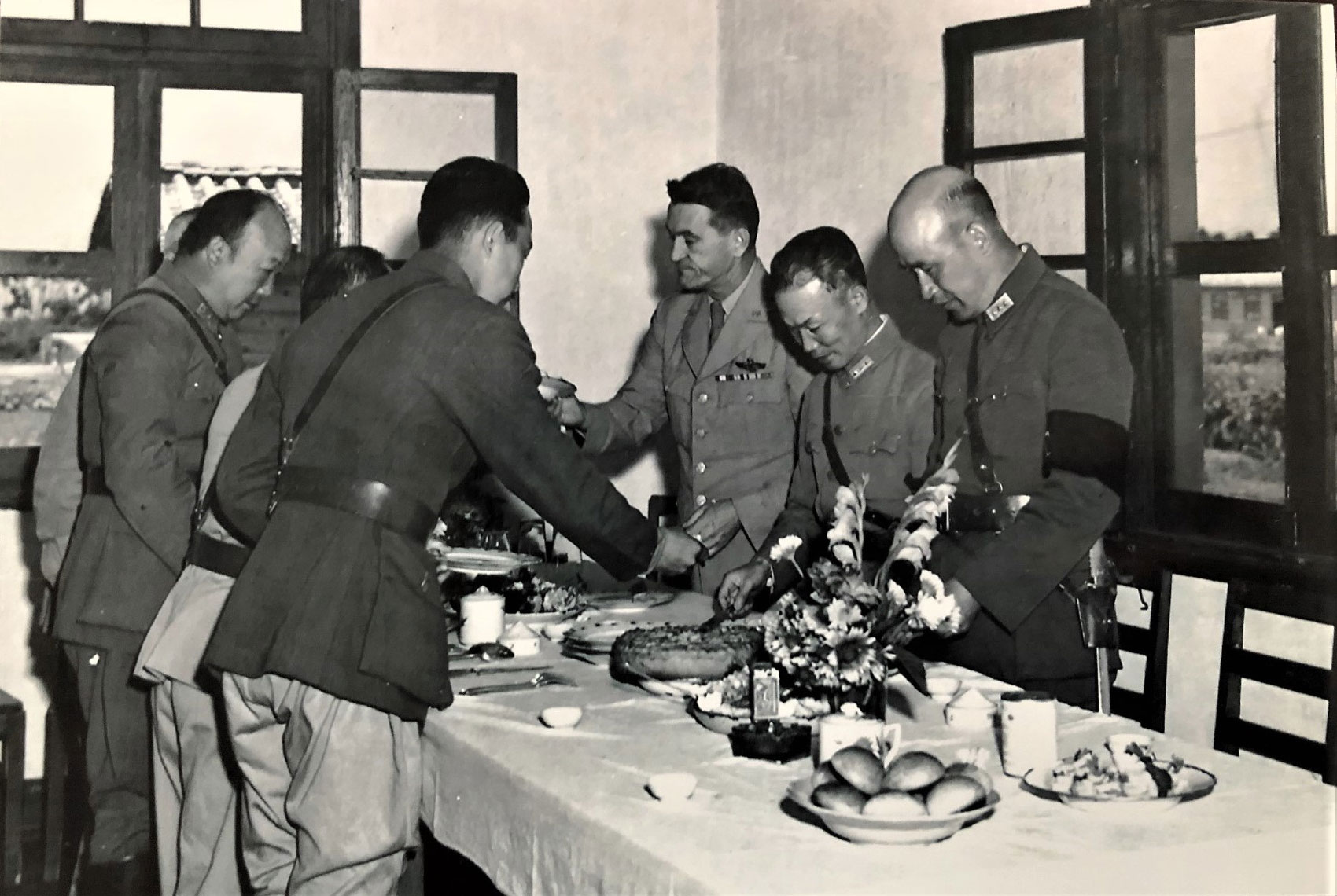 Black and white photo of a group of men in military uniform standing over a dinner table serving food.