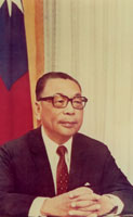 Chiang Ching-kuo sitting at a desk in front of a flag