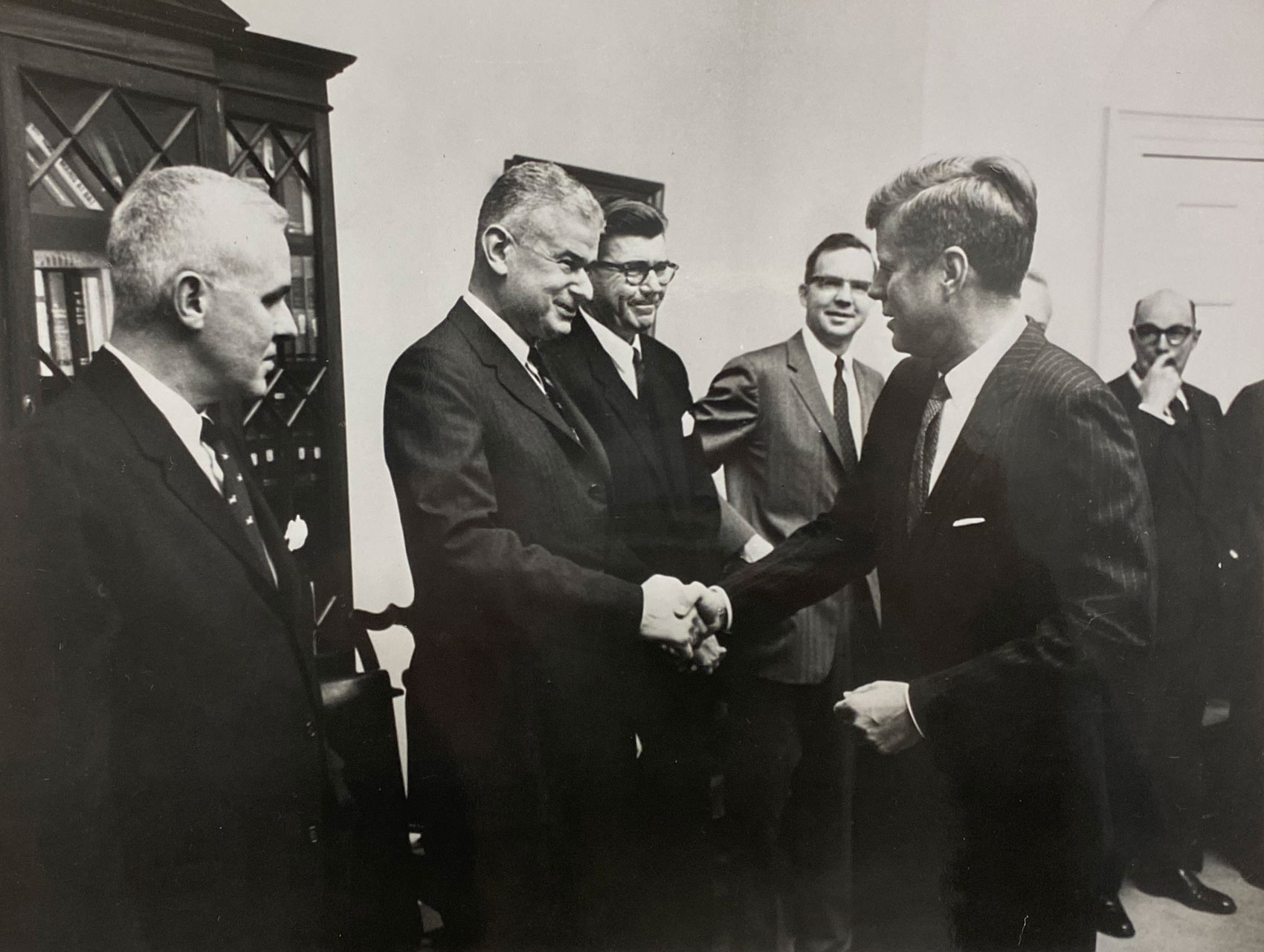 Black and white photo of 5 men in a room. Norman Obbard shaking hands with President John F. Kennedy.