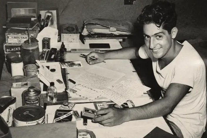 Nat Bellantoni writting a letter at his desk in a tent during World War II