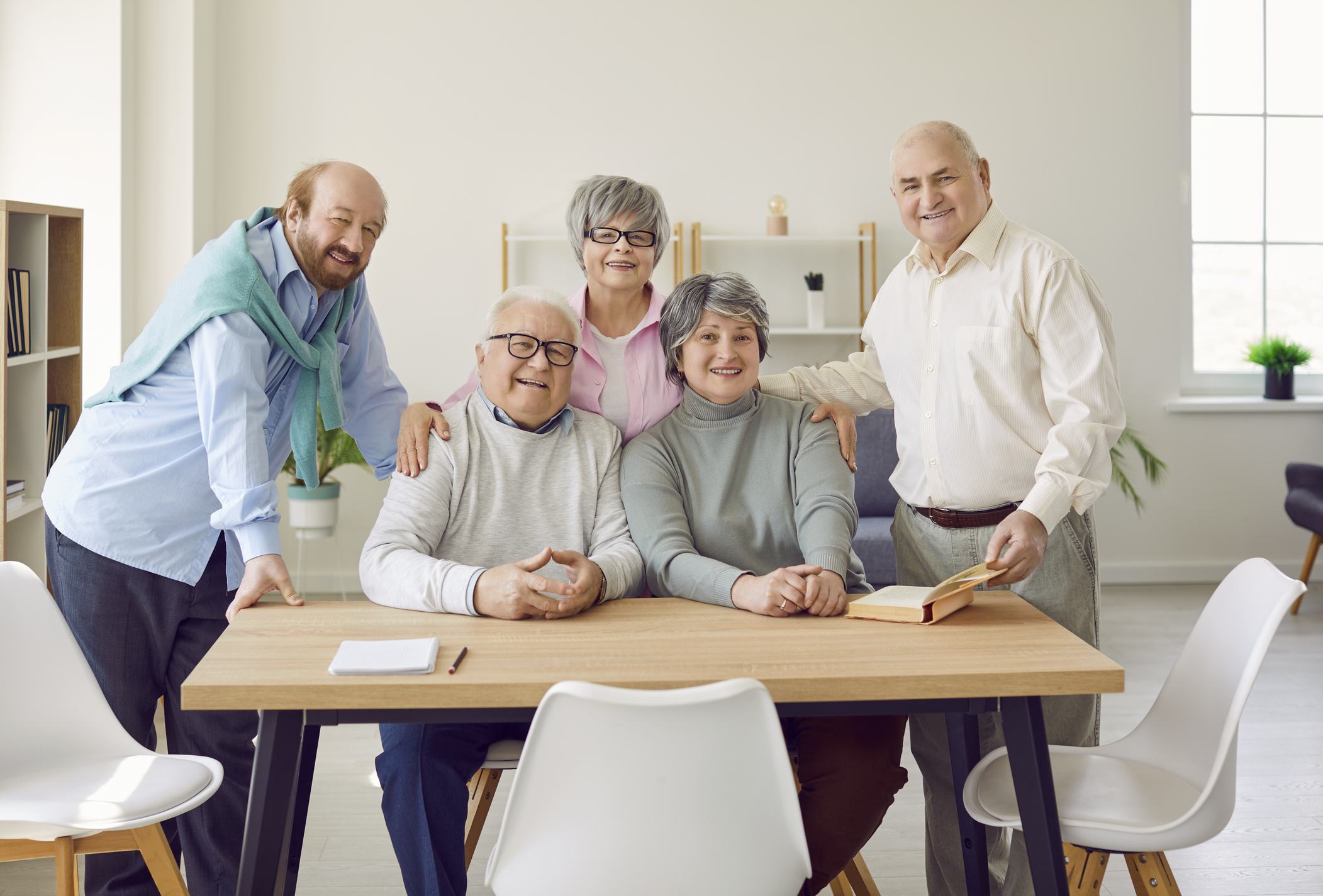 Group of senior people men and women sitting in nursing home at the table and looking at camera. - stock photo