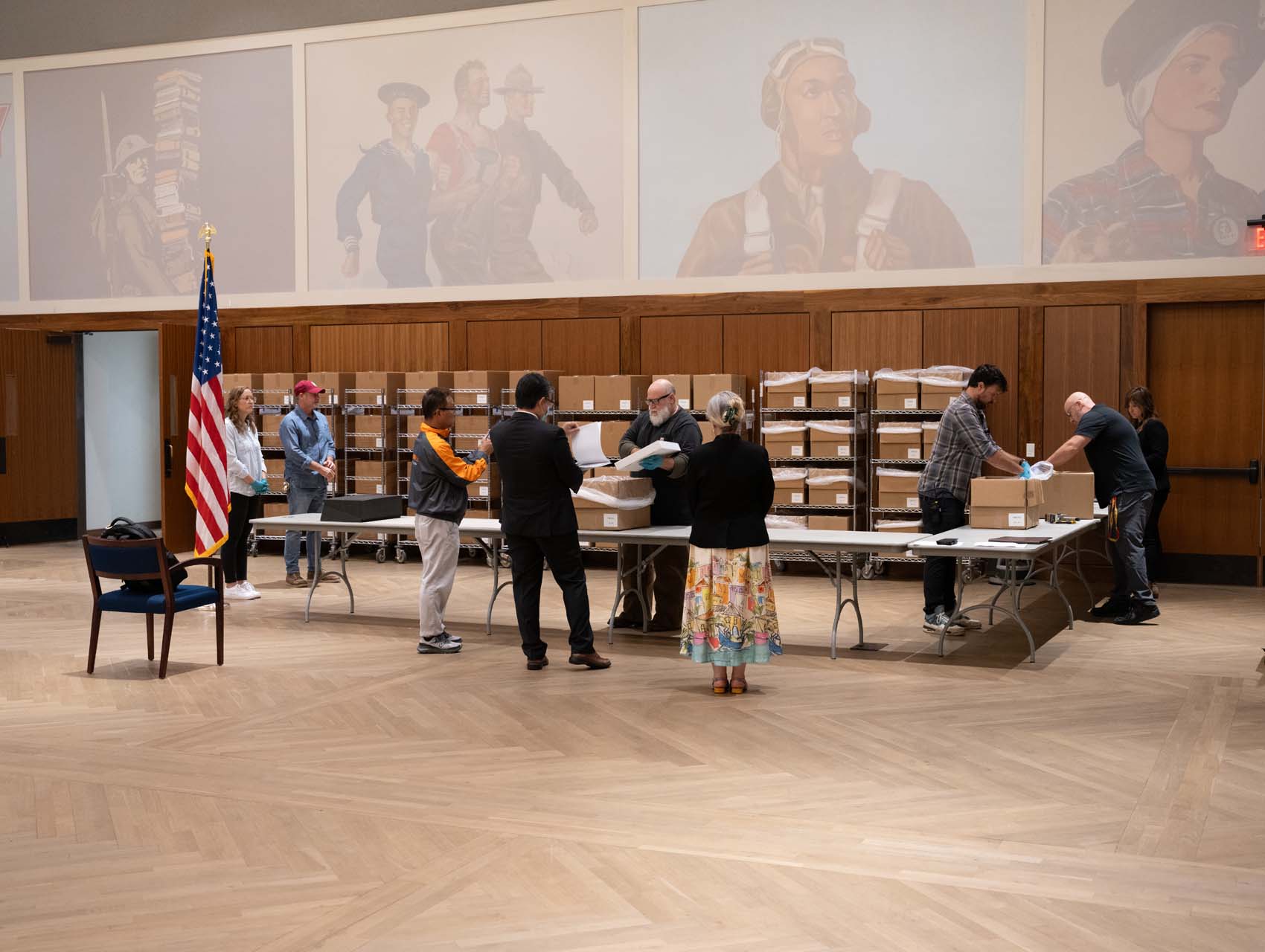 People standing and working around a tables. Boxes on metal shelves in the background