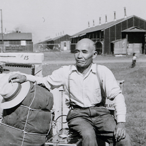 Photograph of a Japanese American man sitting on luggage at an internment camp