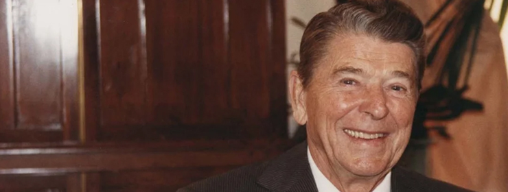Detail of a color photograph showing a smiling President Ronald Reagan in front of wood siding