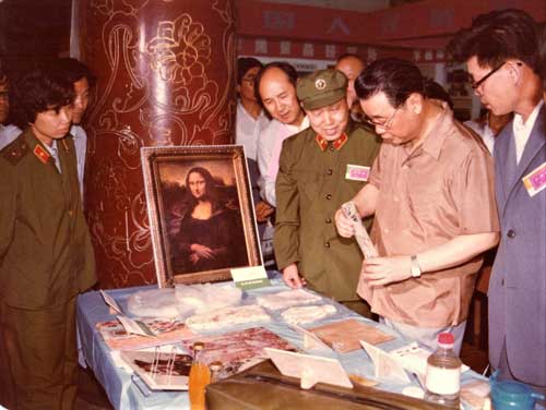 Photograph of Jiang Lin and people standing around a table with objects at an exhibition
