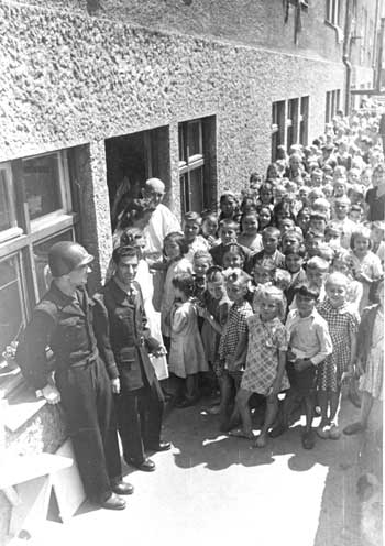 Black and white photo of a group of children and other adults standing next to a building