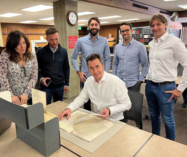 People standing behind person seated at a table handling archival materials