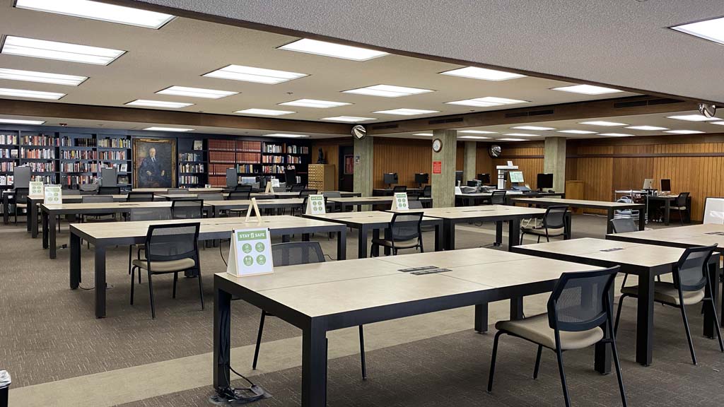 Photo of the Hoover Library &amp; Archives Reading Room with tables, chairs physically distanced, and book shelves