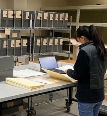 Jessica Y standing in front of a table with documents, laptop, and manuscript boxes