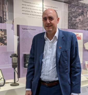 Jamie Fly, president of Radio Free Europe/Radio Liberty visiting Hoover Tower gallery stands next to RFE/FL microphone