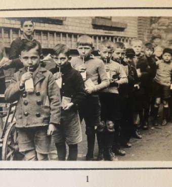 Group of children standing in line drinking from a bottle with a straw