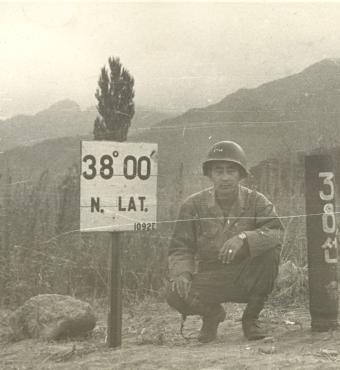 Black and white photo Kay K. Sasaki in US military uniform posing next to 38' 00" N. Lat. sign