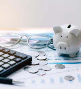 Piggy bank, coins, glasses, and calculator on top of paper