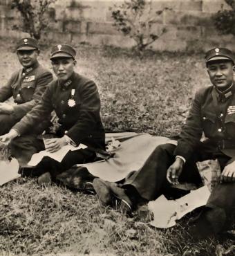 Black and white photo of 3 men dressed in military uniforms sitting on the ground having a picnic.