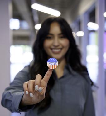 Young Hispanic Woman in Her Twenties Proudly Displaying Her I Voted Sticker in a Co-Working Space stock photo