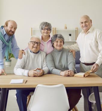 Group of senior people men and women sitting in nursing home at the table and looking at camera. - stock photo