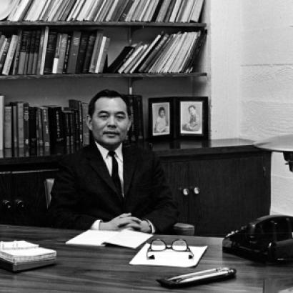 Black and white photo of Eugene Wu sitting at a desk with a bookshelf in the background