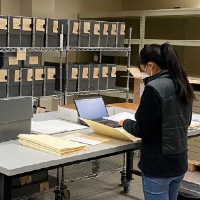 Jessica Y standing in front of a table with documents, laptop, and manuscript boxes