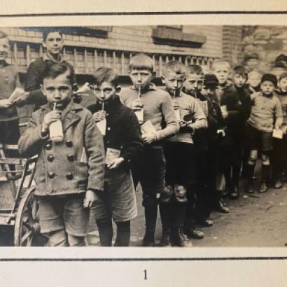 Group of children standing in line drinking from a bottle with a straw