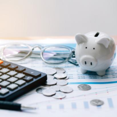 Piggy bank, coins, glasses, and calculator on top of paper