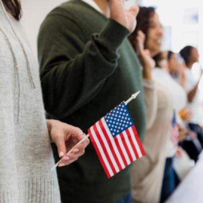 The group of multiracial people stand and raise their hand to say the pledge.