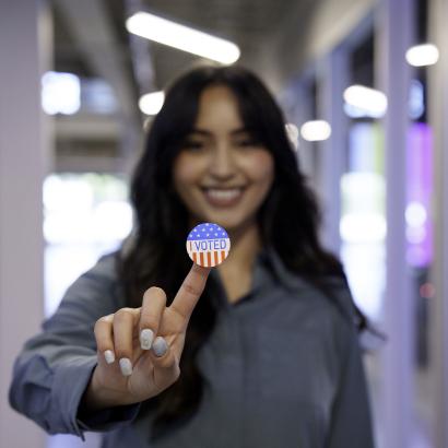 Young Hispanic Woman in Her Twenties Proudly Displaying Her I Voted Sticker in a Co-Working Space stock photo
