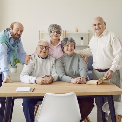 Group of senior people men and women sitting in nursing home at the table and looking at camera. - stock photo
