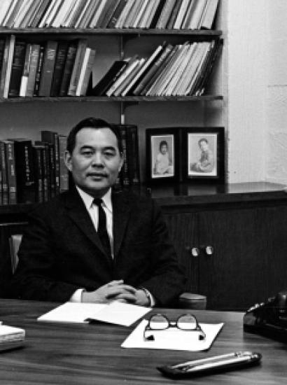 Black and white photo of Eugene Wu sitting at a desk with a bookshelf in the background