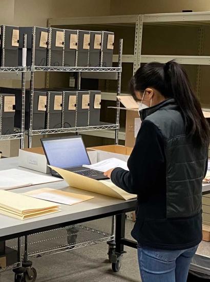 Jessica Y standing in front of a table with documents, laptop, and manuscript boxes