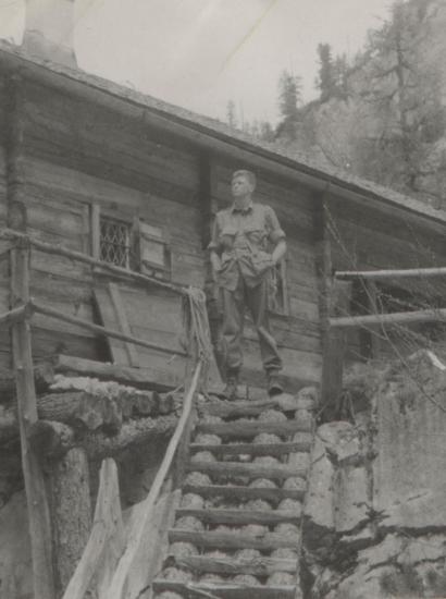 US soldier Donald Wayne Richardson standing in front of a log cabin.