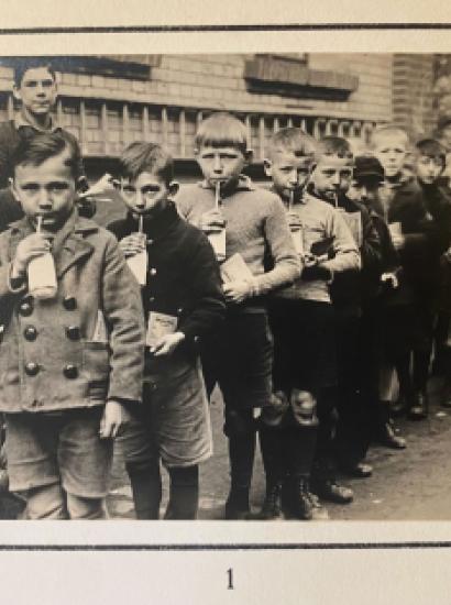 Group of children standing in line drinking from a bottle with a straw