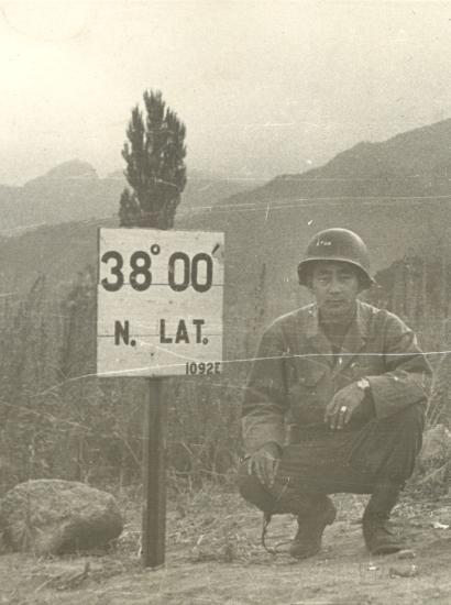 Black and white photo Kay K. Sasaki in US military uniform posing next to 38' 00" N. Lat. sign