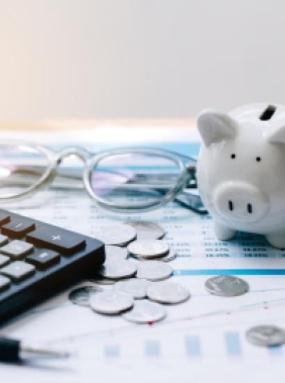 Piggy bank, coins, glasses, and calculator on top of paper