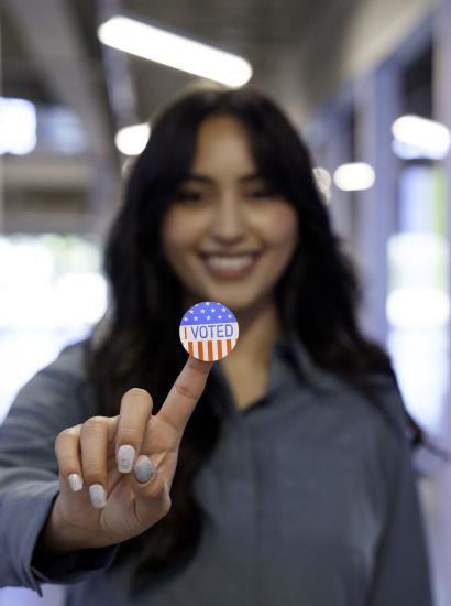 Young Hispanic Woman in Her Twenties Proudly Displaying Her I Voted Sticker in a Co-Working Space stock photo