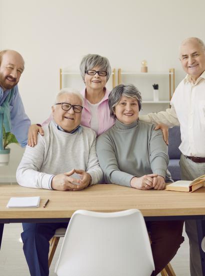 Group of senior people men and women sitting in nursing home at the table and looking at camera. - stock photo