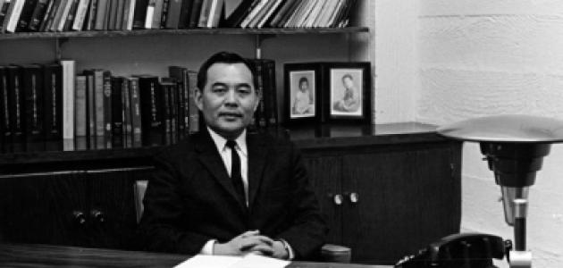 Black and white photo of Eugene Wu sitting at a desk with a bookshelf in the background