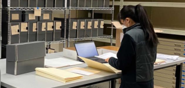 Jessica Y standing in front of a table with documents, laptop, and manuscript boxes