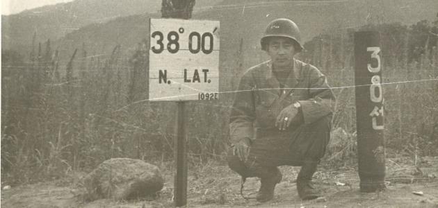 Black and white photo Kay K. Sasaki in US military uniform posing next to 38' 00" N. Lat. sign