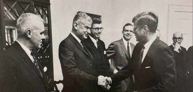 Black and white photo of 5 men in a room. Norman Obbard shaking hands with President John F. Kennedy.