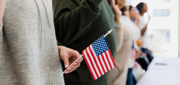 The group of multiracial people stand and raise their hand to say the pledge.