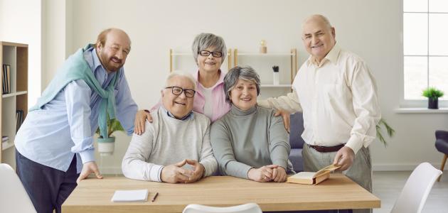 Group of senior people men and women sitting in nursing home at the table and looking at camera. - stock photo