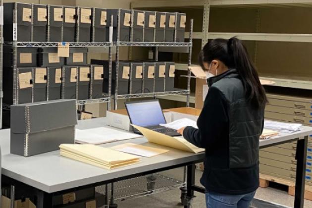 Jessica Y standing in front of a table with documents, laptop, and manuscript boxes