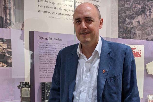 Jamie Fly, president of Radio Free Europe/Radio Liberty visiting Hoover Tower gallery stands next to RFE/FL microphone